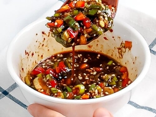 Korean flavored soy sauce made with peppers, green onions, and sesame seeds being mixed with a spoon.