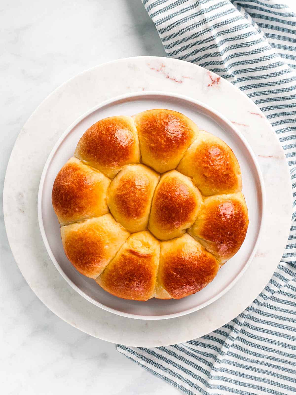 Buttery brioche rolls baked in a round pan on a white plate.