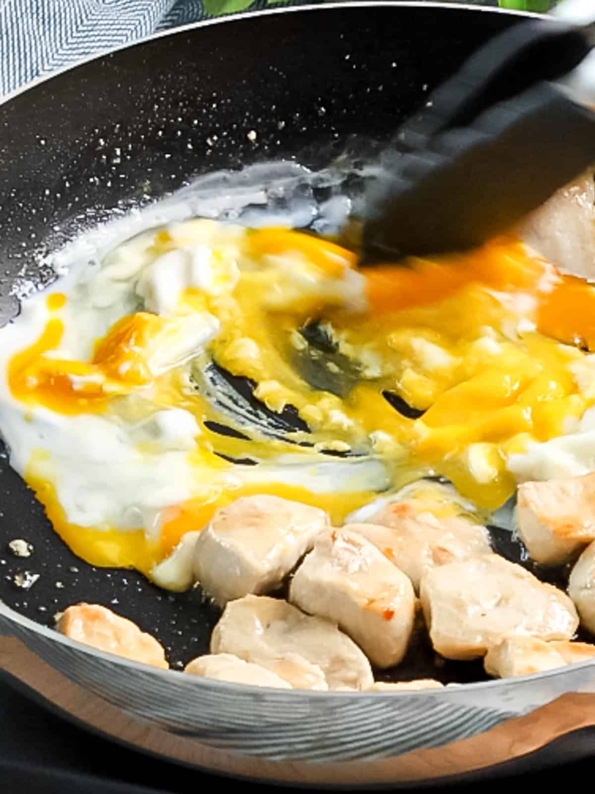 Frying and scrambling eggs in a pan with chicken.