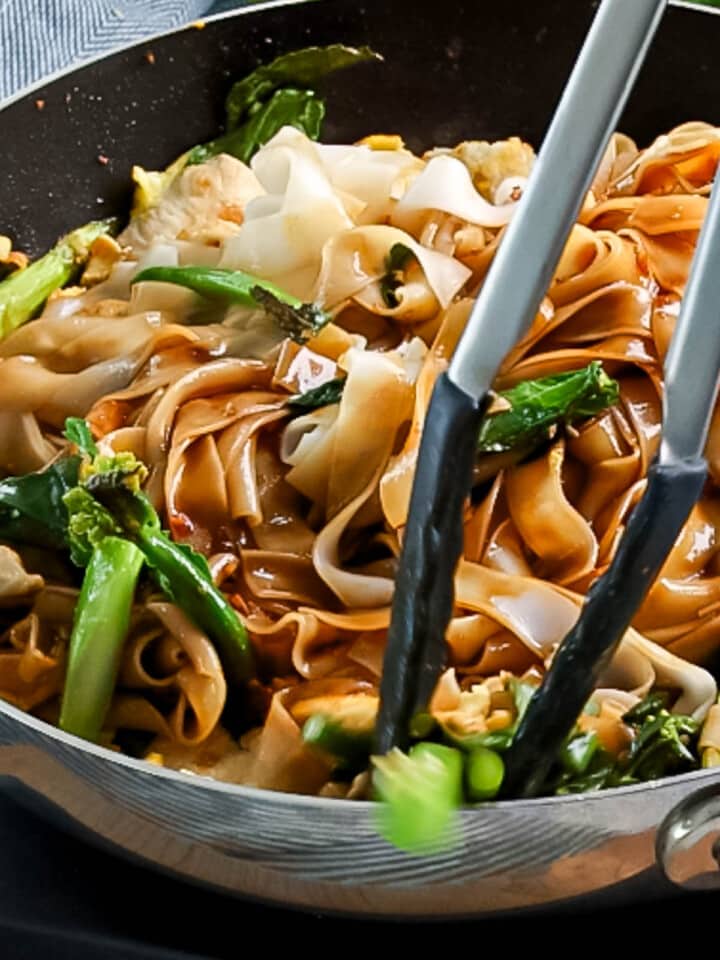 Wide rice noodles and Chinese broccoli being tossed together with pad see ew sauce until mixed together.