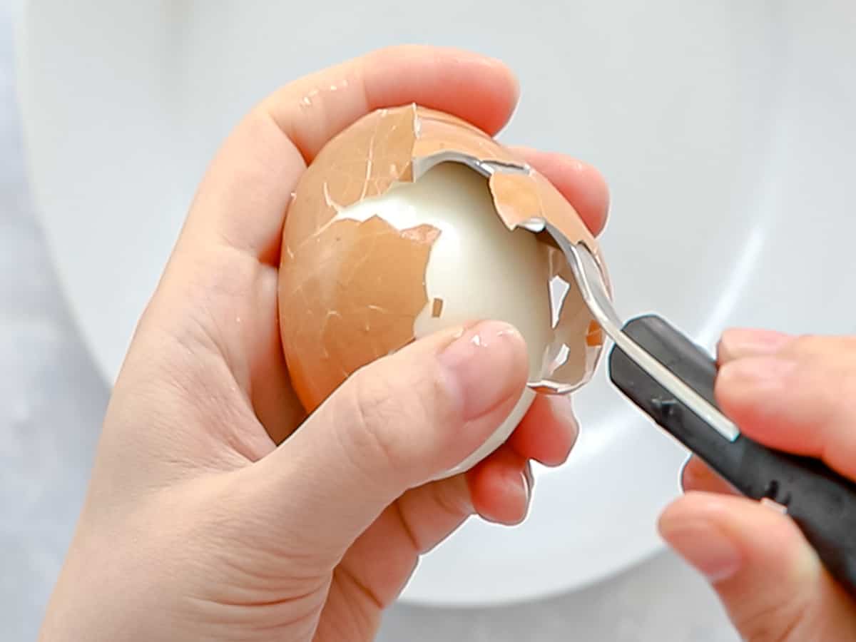 Spoon being inserted between a soft boiled egg and the shell for easy peeling.