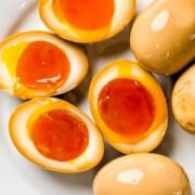 Ramen eggs or soy sauce eggs cut in half on a plate with text overlay with red background.