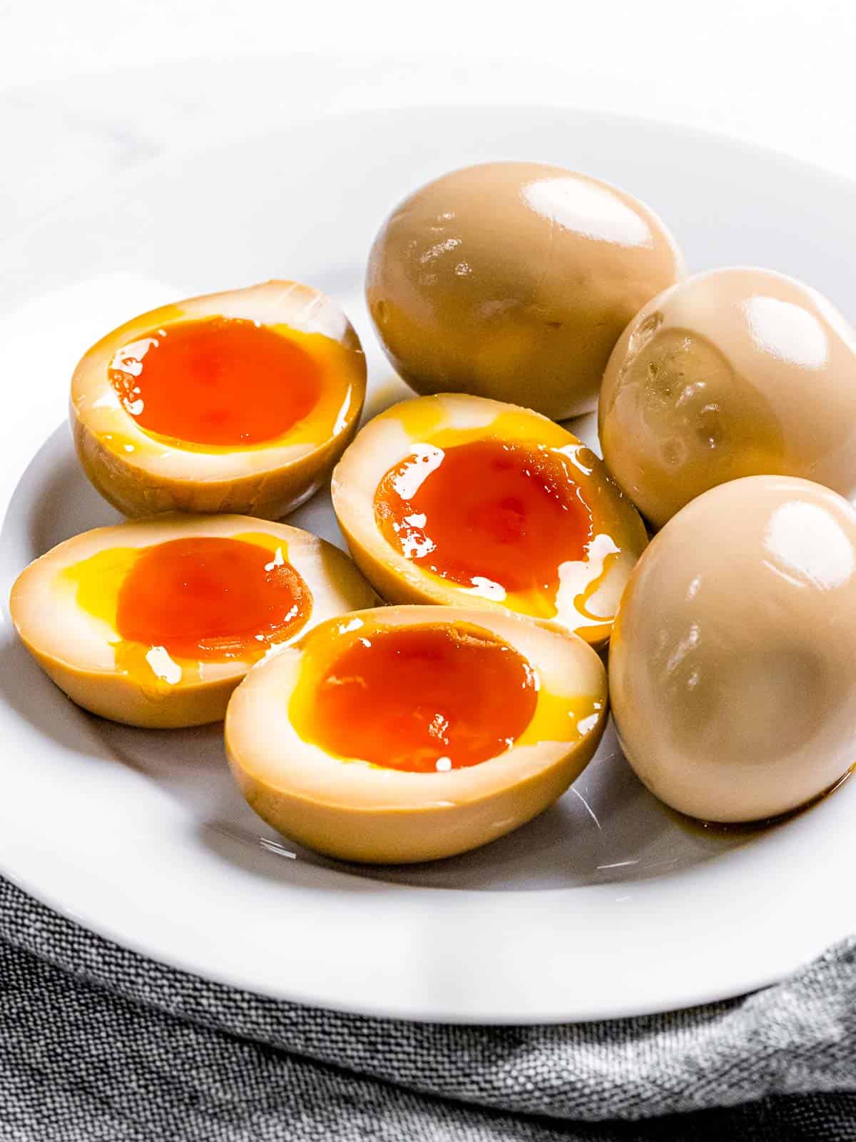 Ramen eggs marinated in soy sauce with soft boiled yolk cut in half to show orange, runny yolk on a plate.