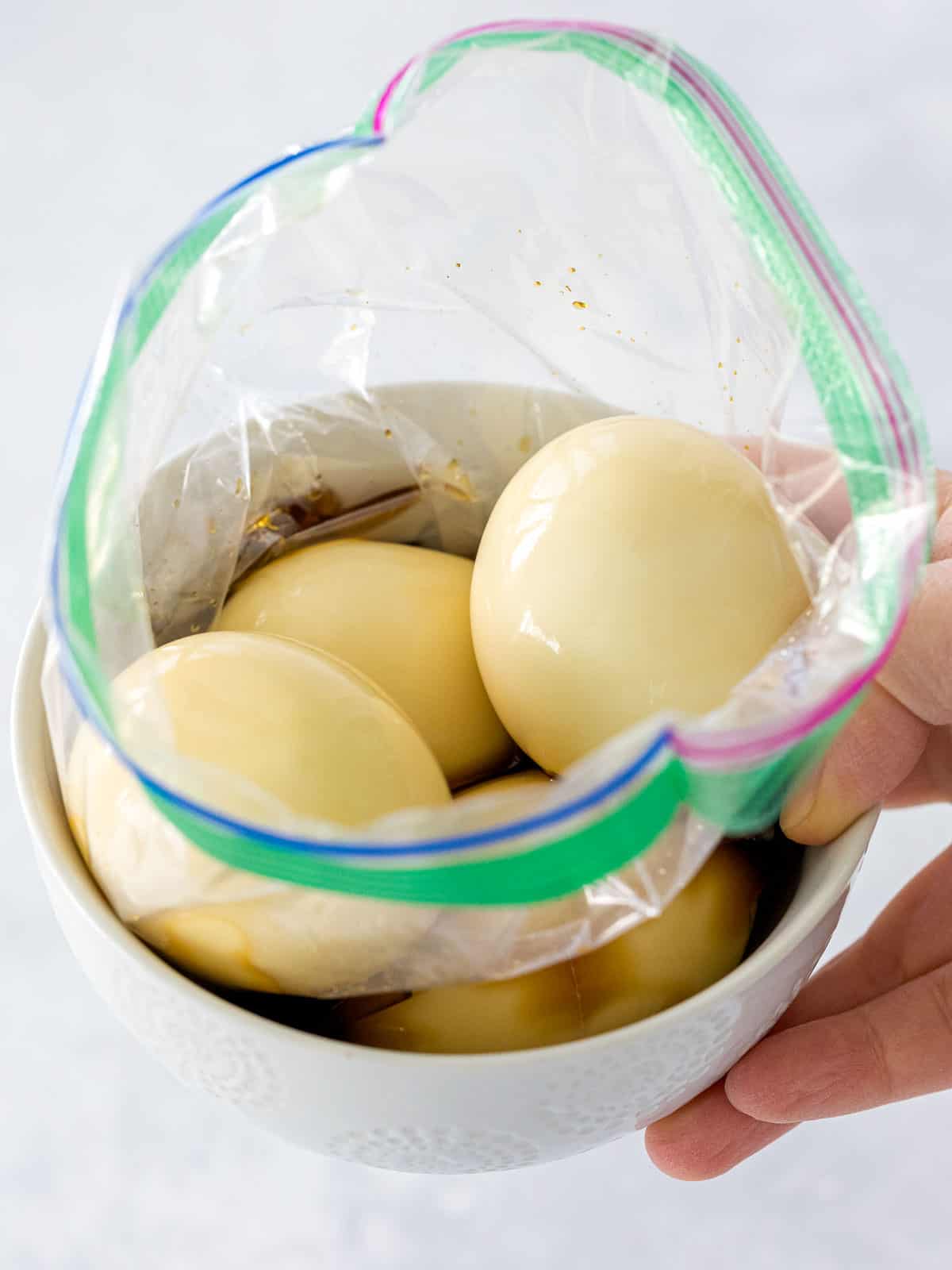 Soft boiled eggs in a soy sauce and mirin marinade inside a plastic bag set in a small bowl.