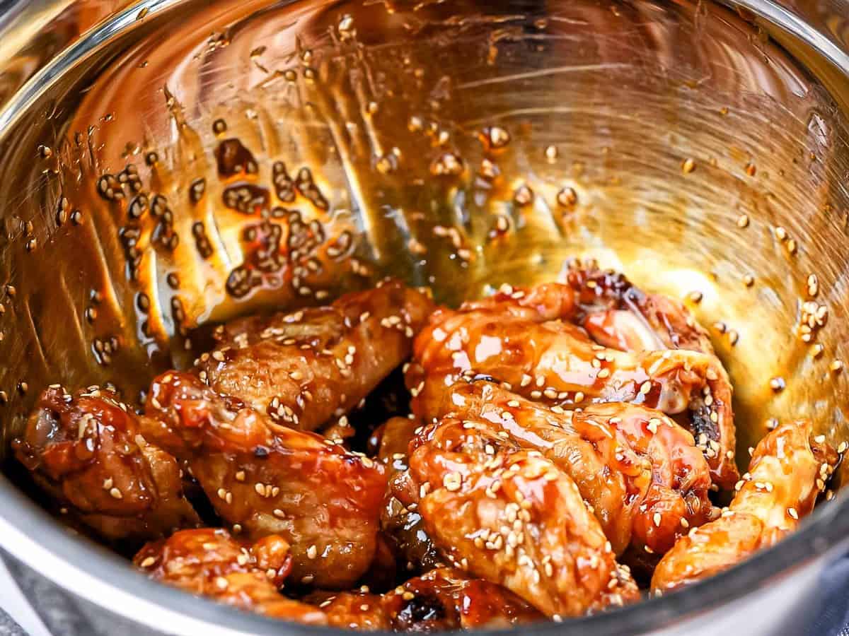 Baked chicken wings tossed with wing sauce in a metal bowl.