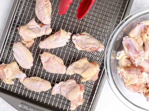 Uncooked chicken wings being placed on a baking sheet lined with a baking rack.