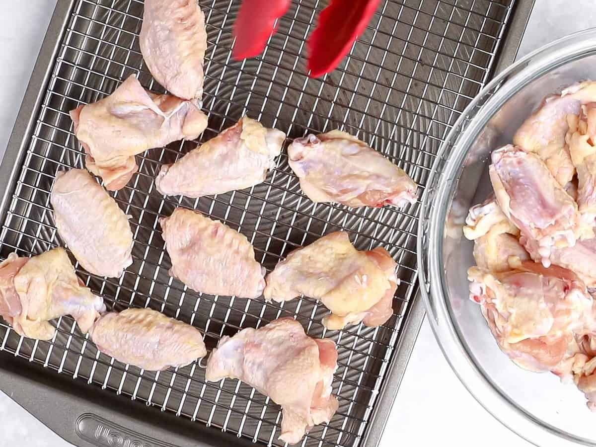 Uncooked chicken wings being placed on a baking sheet lined with a wire rack.