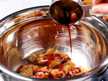 Wing sauce being poured onto crispy baked chicken wings in a metal bowl.