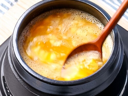 Egg mixture being stirred with a spoon and cooking in a ttukbaegi.