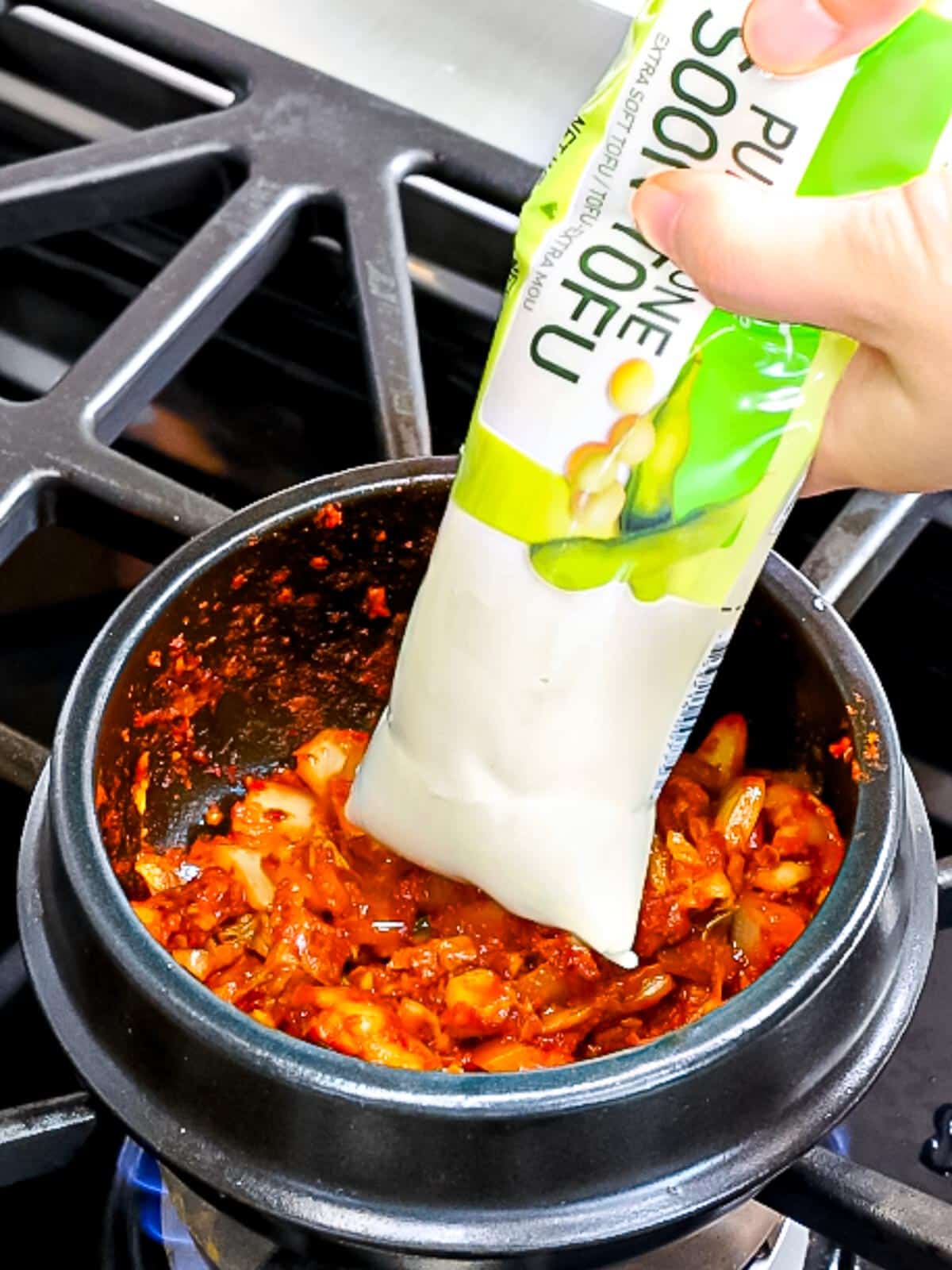 Korean soft tofu being added to kimchi in an earthenware pot.