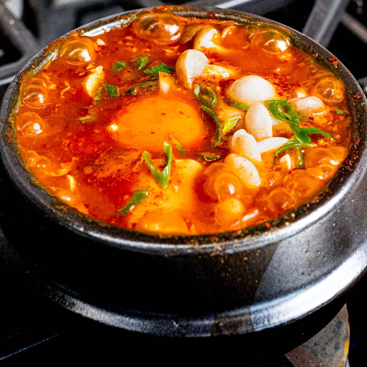 Soondubu jjigae with mushrooms, soft tofu, and egg cooking in an earthenware pot.