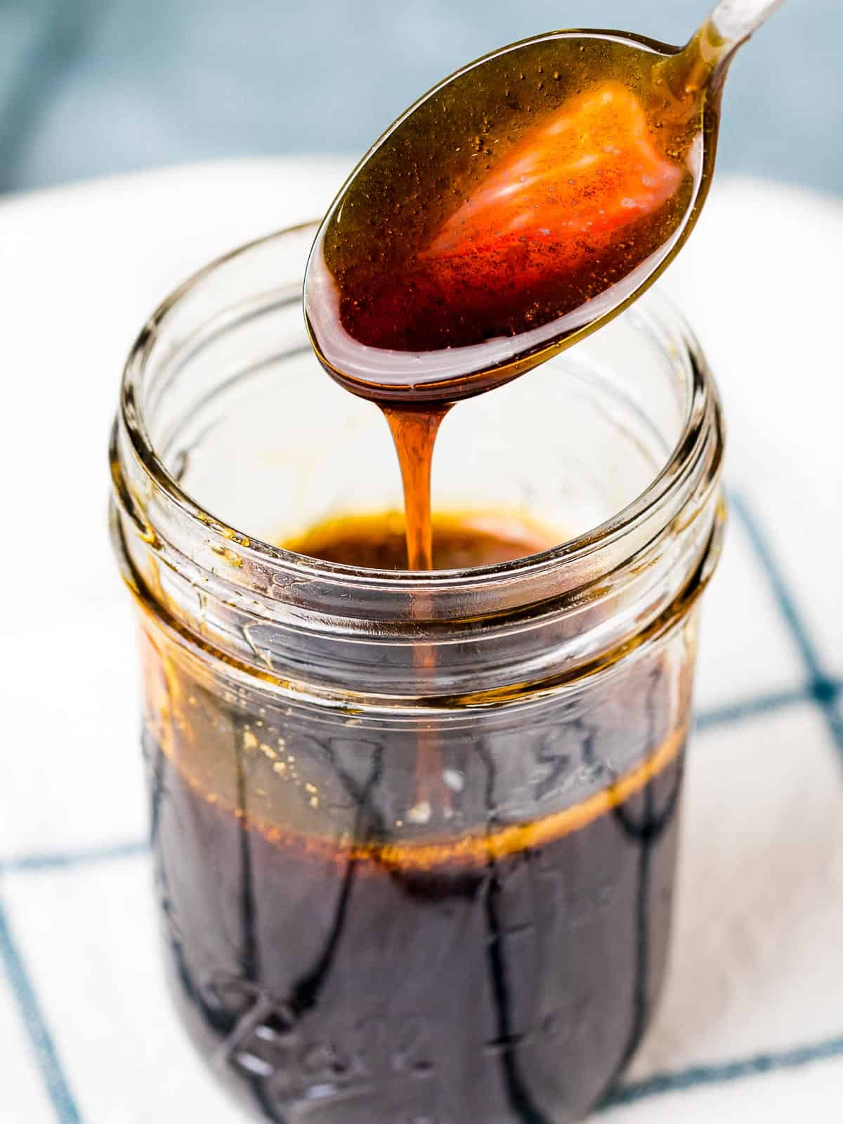 Homemade teriyaki sauce dripping off a spoon into a jar.