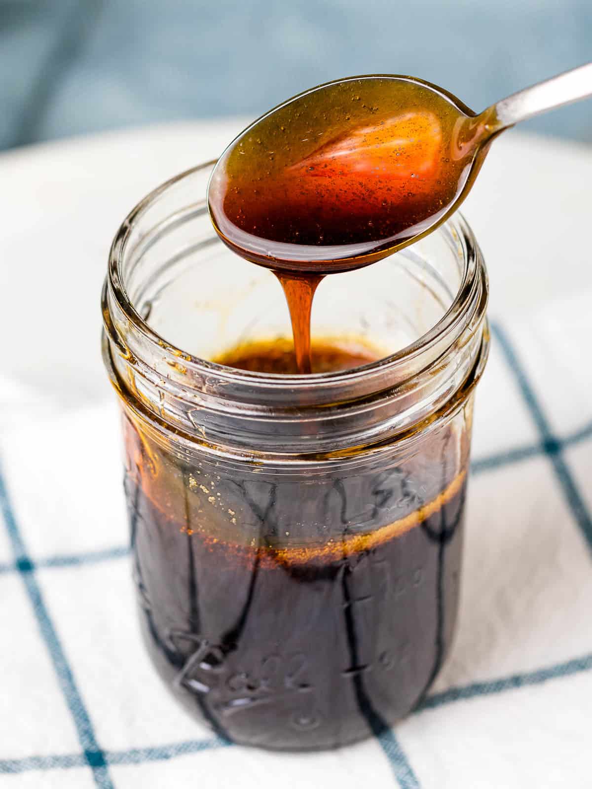 Thick homemade teriyaki sauce pouring off a spoon into a glass jar.