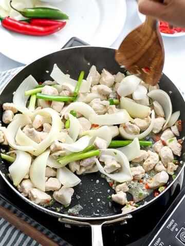 Chicken, onions, and green onions stir frying in a pan.
