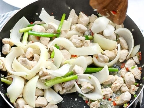 Chicken, onions, and green onions stir frying in a pan.