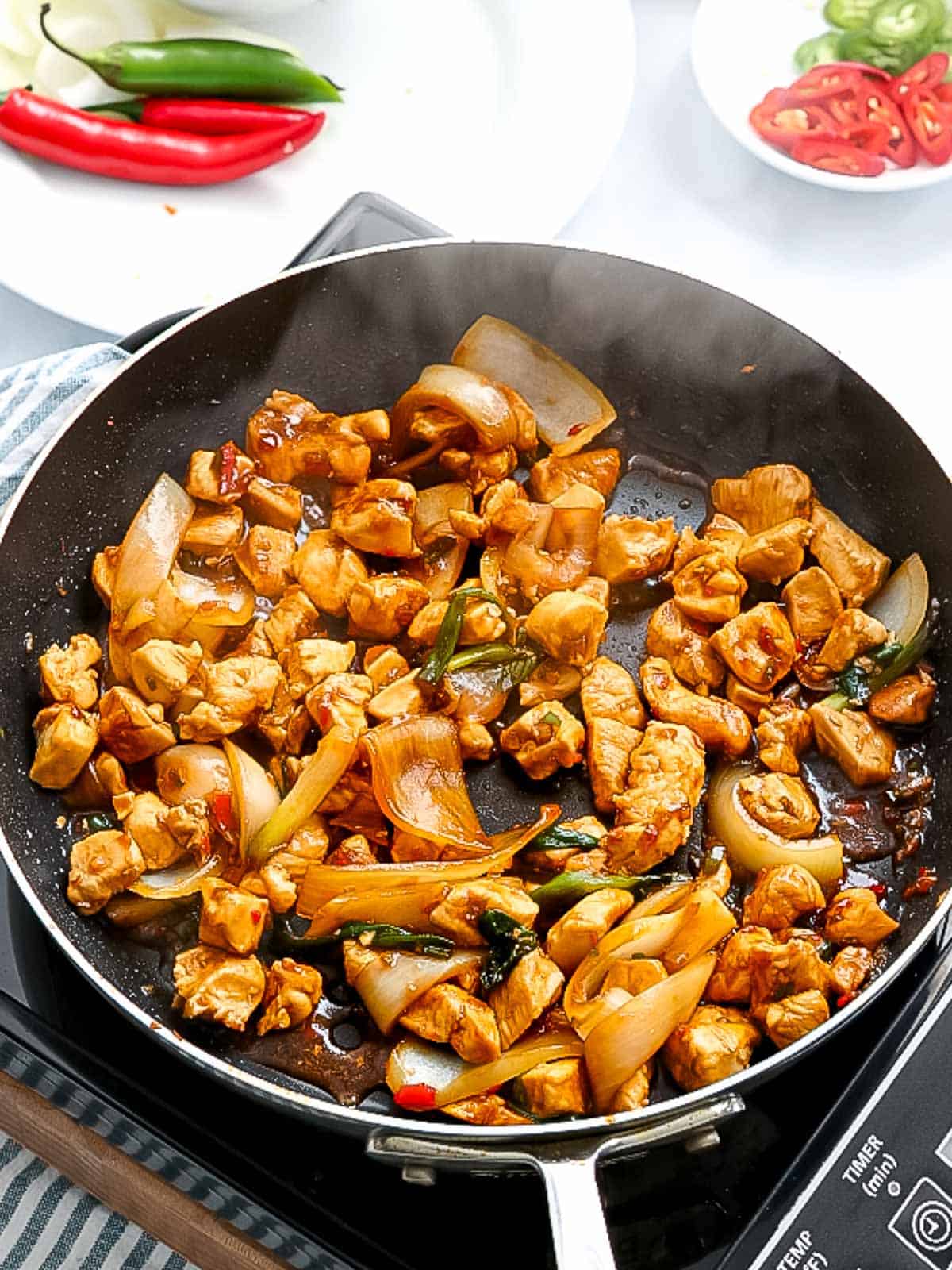 Chicken stir frying in a pan with sauce.
