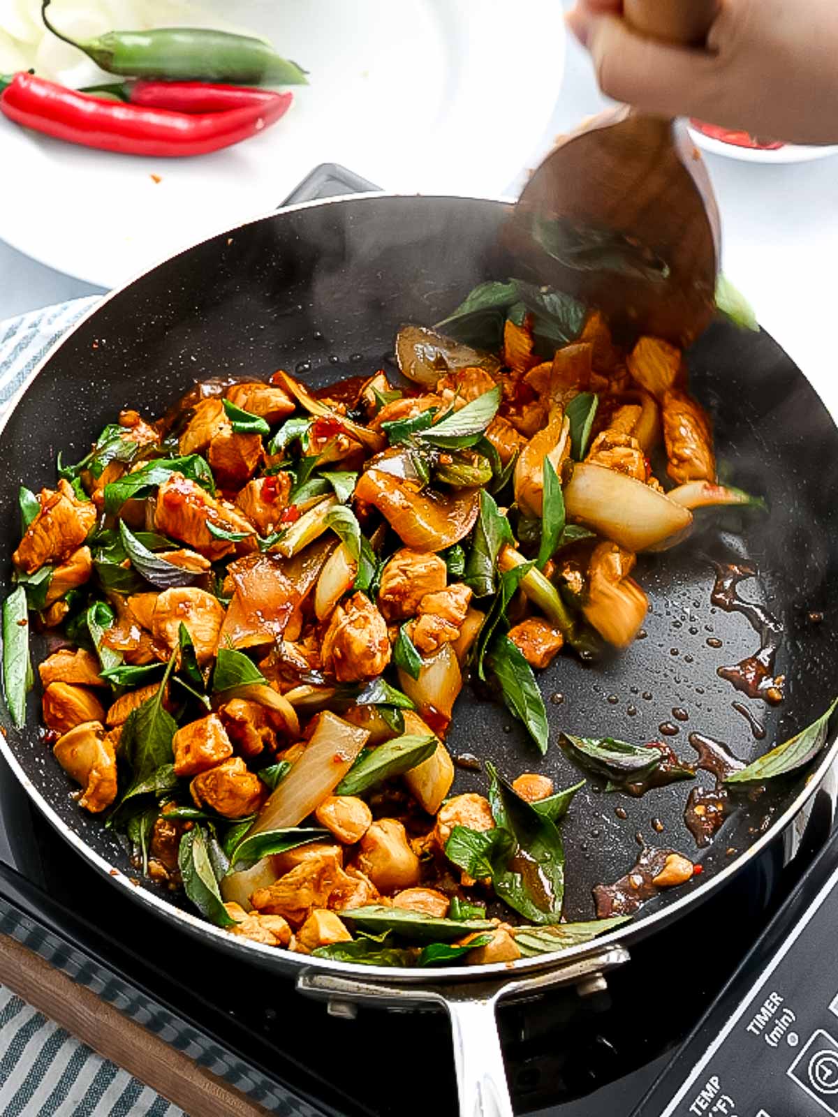 Thai basil stir frying with chicken in a pan.