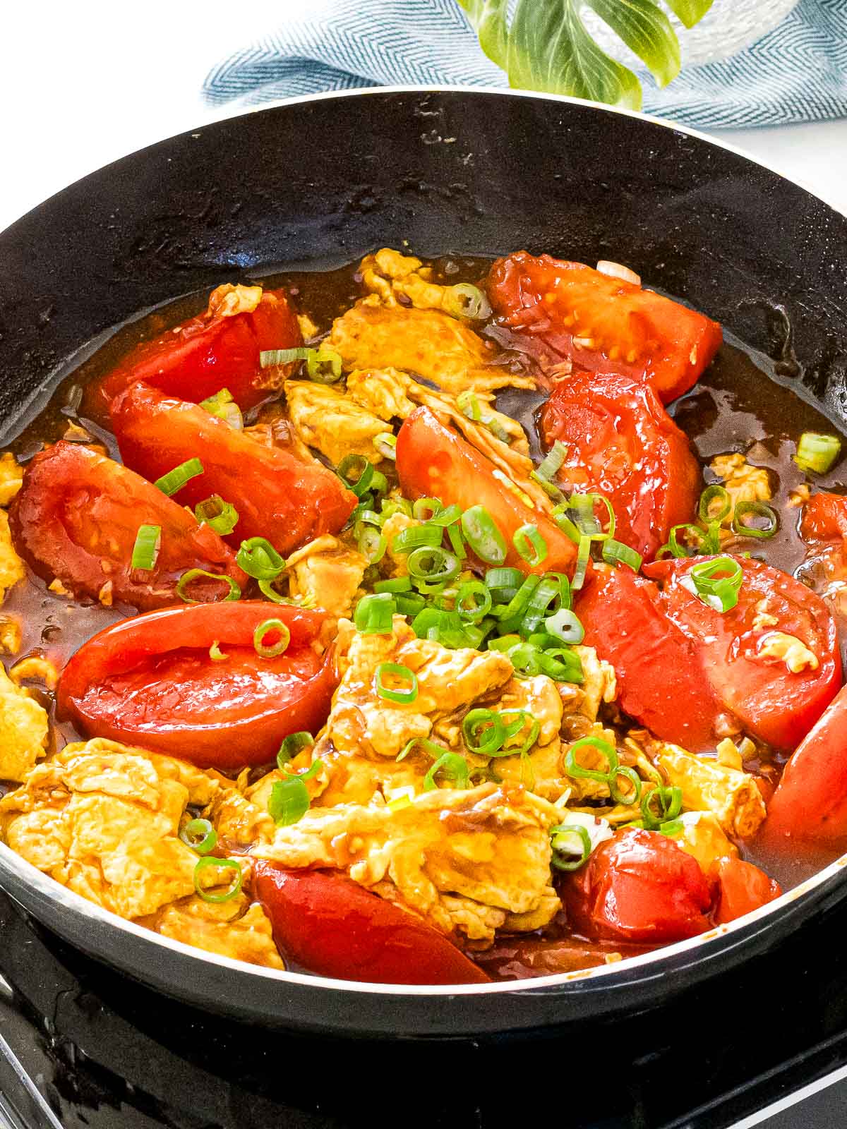 Chinese tomato egg stir fry in a pan with juicy red tomatoes and scrambled eggs with green onions.