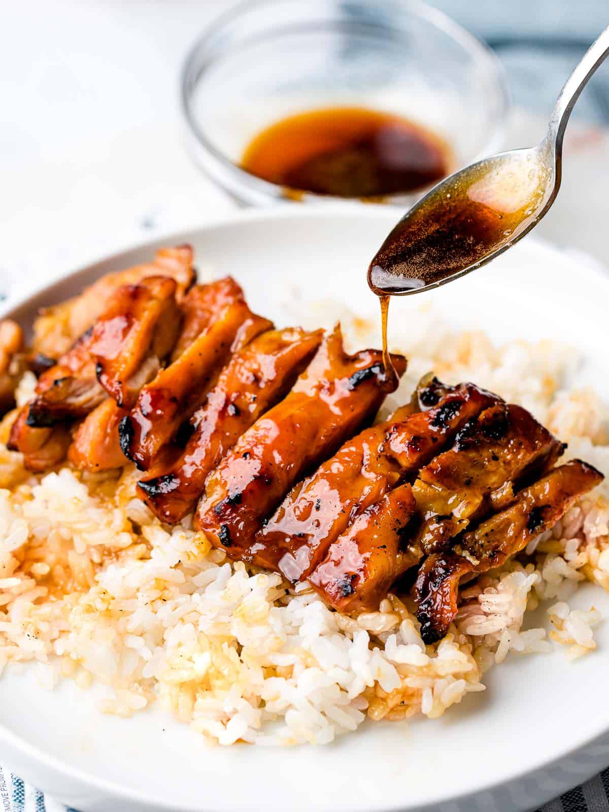 Chicken teriyaki being glazed with sauce with steamed rice.