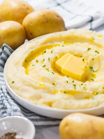 Instant pot mashed potatoes with butter and chives next to Yukon gold potatoes.