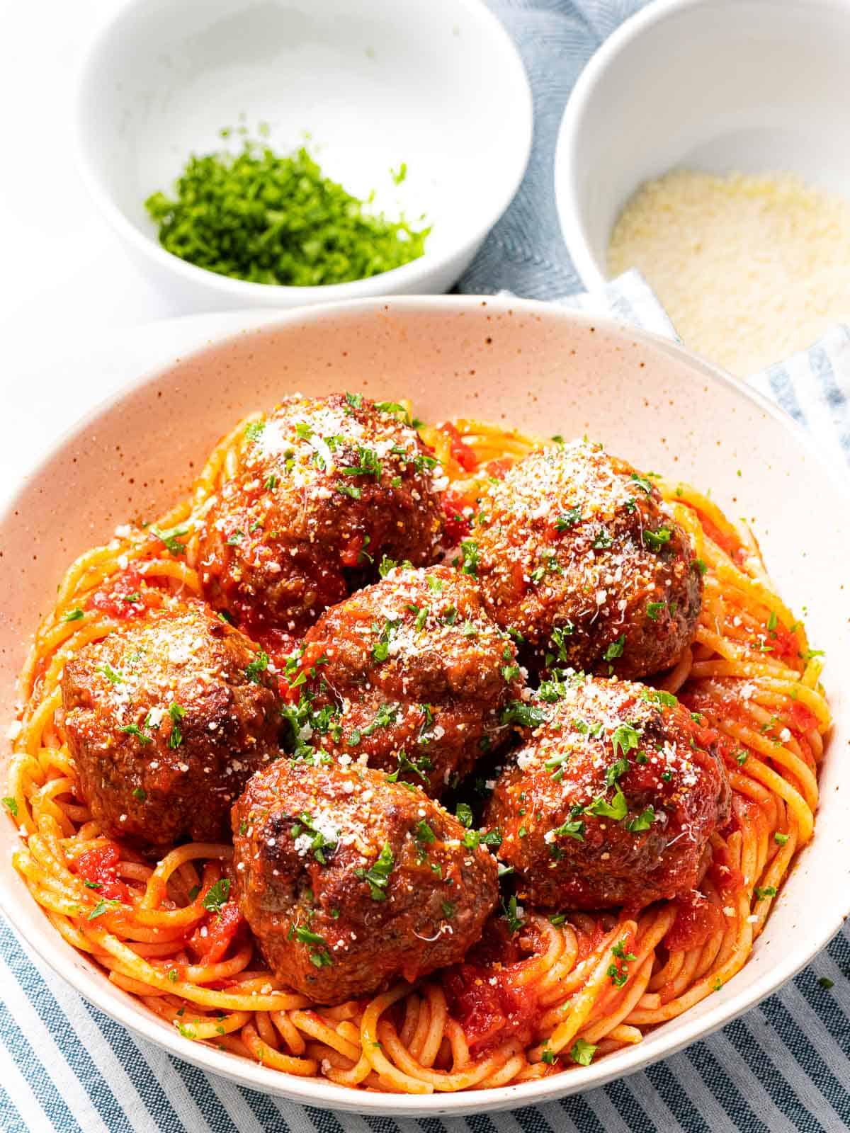 Italian meatballs with spaghetti next to parmesan cheese and parsley.