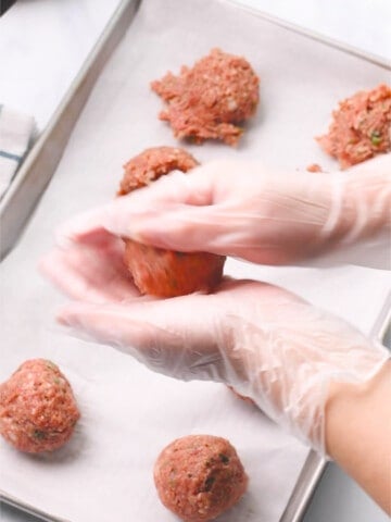 Rolling and shaping meatballs with hands.