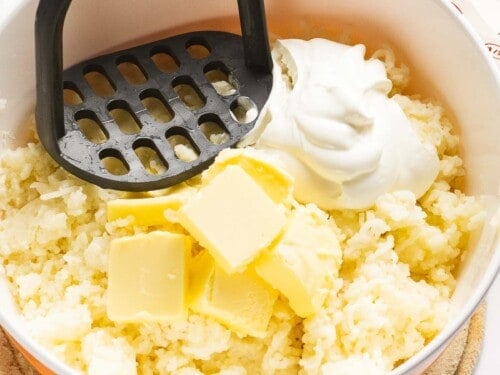 Mashed potatoes with sour cream and butter being mashed with a potato masher.