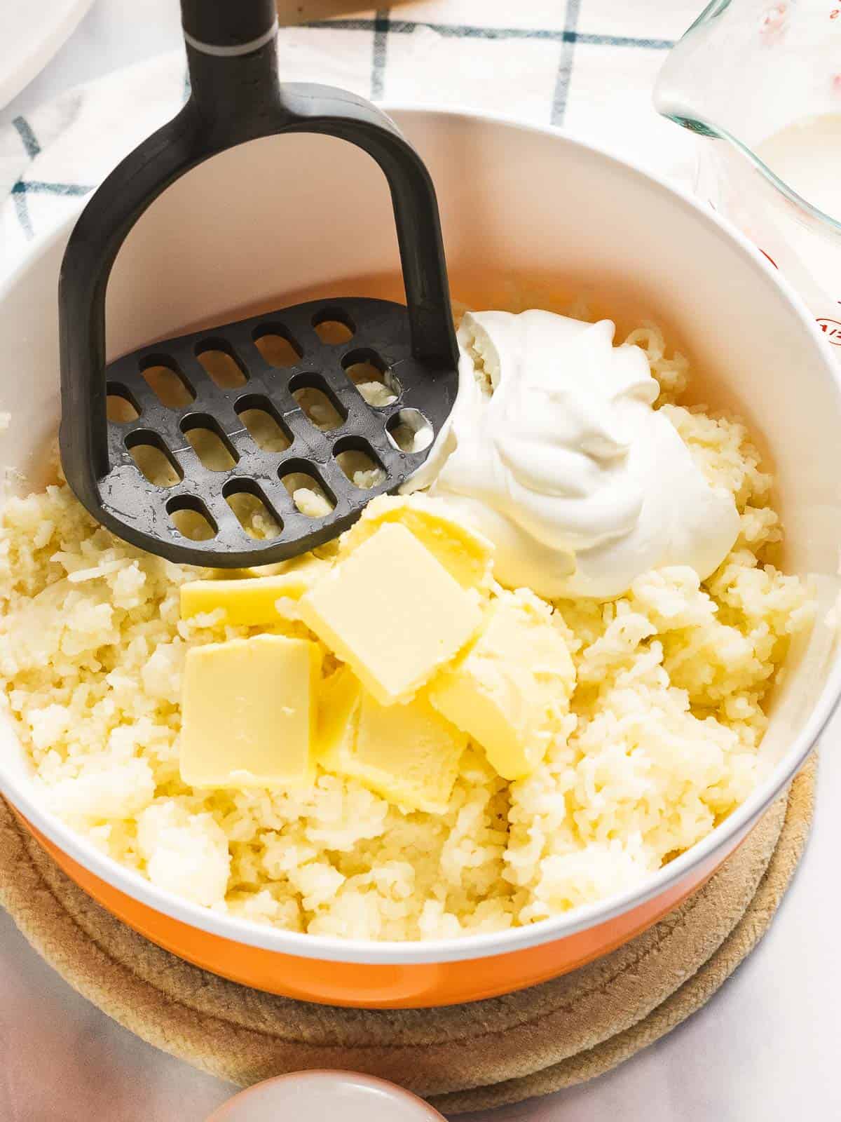 Yukon gold mashed potatoes with sour cream and butter being mashed with a potato masher.