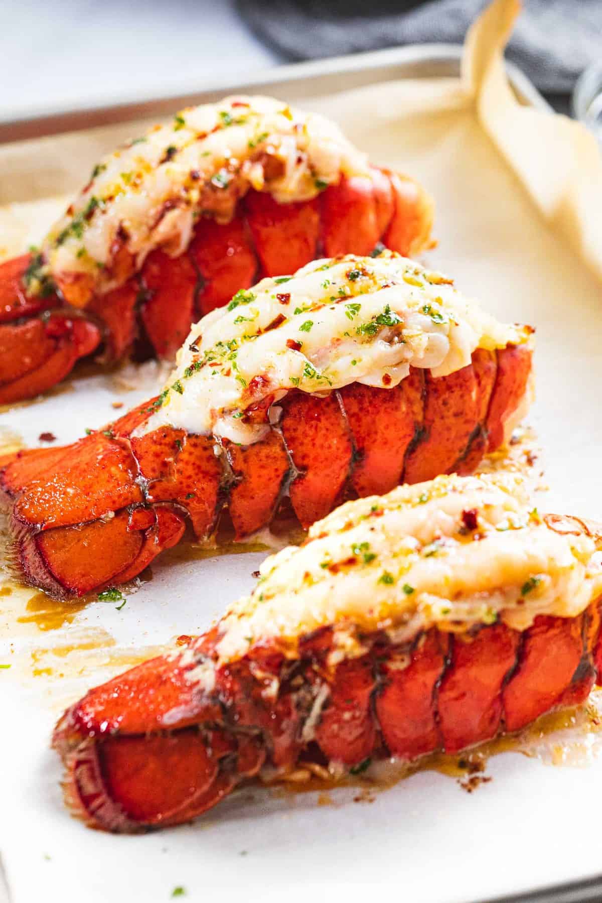 Broiled lobster tails with garlic butter on a baking tray.
