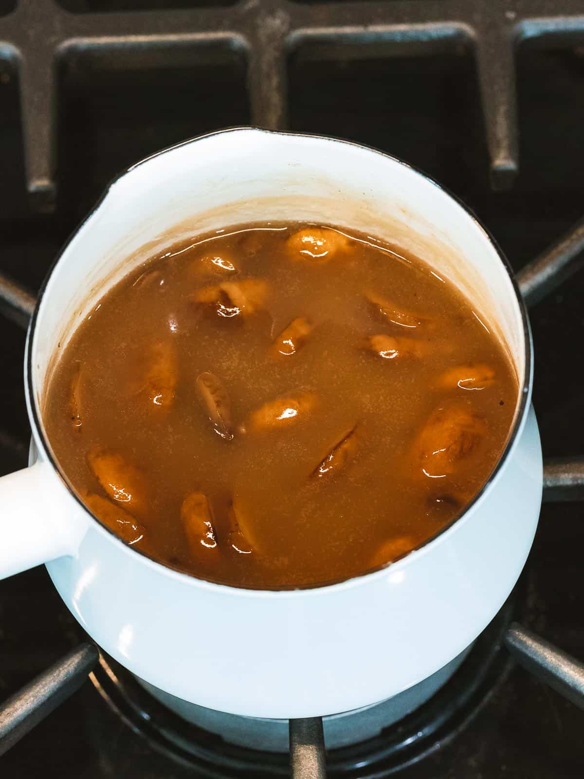 Mushroom gravy with added mushrooms cooking in a pot.