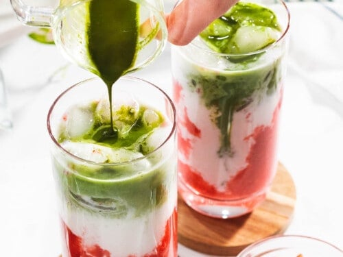 Green matcha poured into two glasses with milk and strawberries.