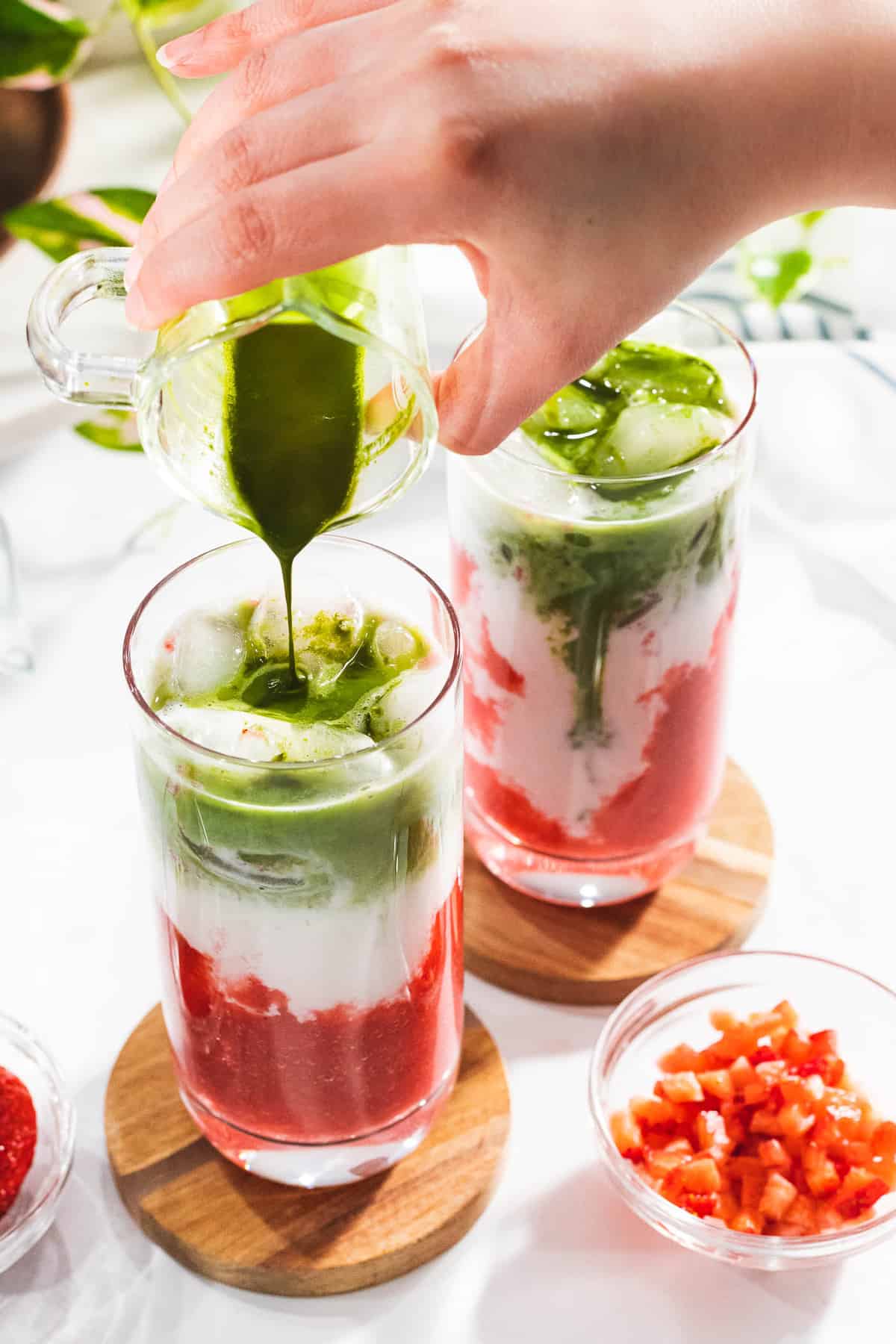 Green matcha poured into two glasses with milk and strawberries.