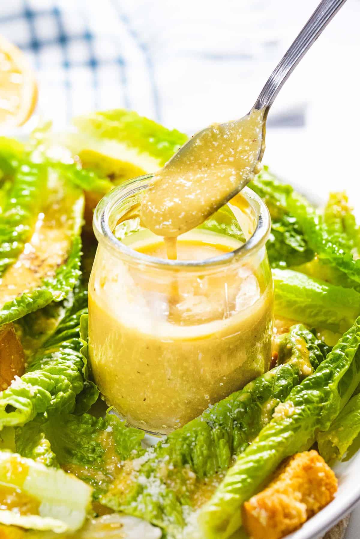 Homemade Caesar salad dressing dripping off a spoon next to romaine lettuce.