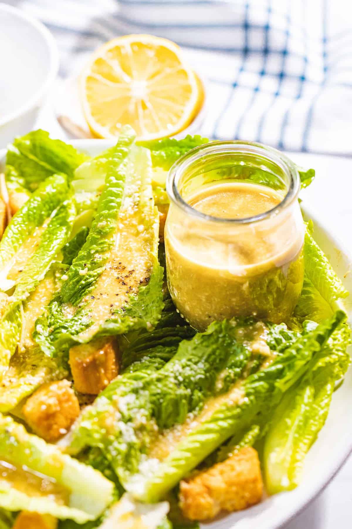 Homemade Caesar salad dressing next to romaine lettuce, croutons, and lemon.