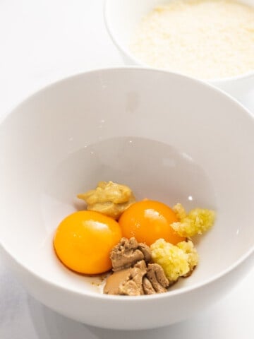Egg yolks, anchovy paste, garlic, and dijon mustard in a bowl.