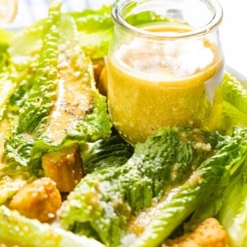 Homemade Caesar salad dressing in a jar next to romaine lettuce.