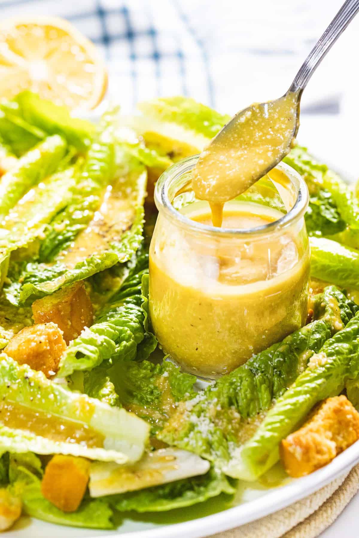 Homemade Caesar salad dressing dripping off a spoon on a plate of romaine lettuce.