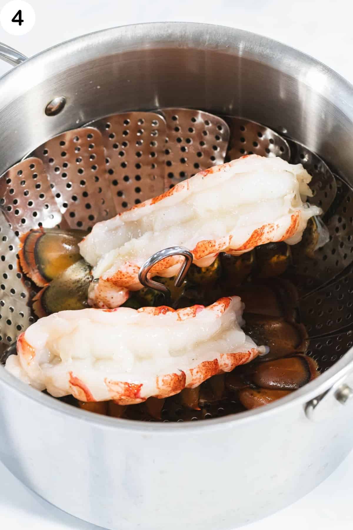 Butterflied lobster tails in a steaming pot with a steaming basket.