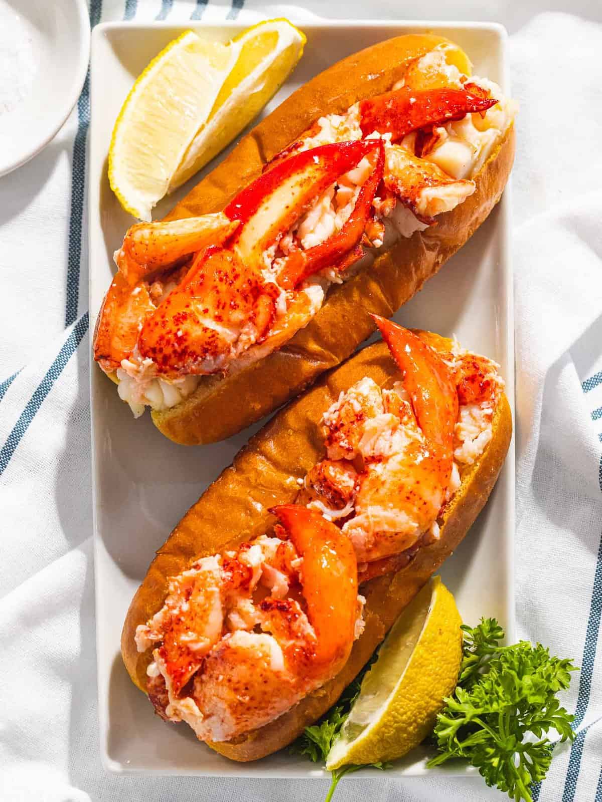 Two lobster rolls on a plate with lemons.