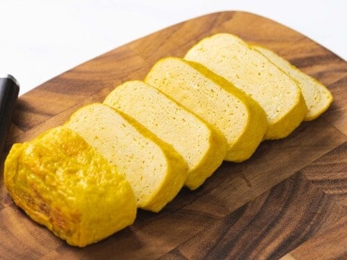 Tamagoyaki omelet cut into thick slices on a wooden cutting board.
