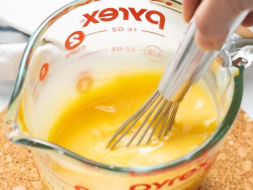 Eggs beaten with a whisk in a measuring cup with a spout.