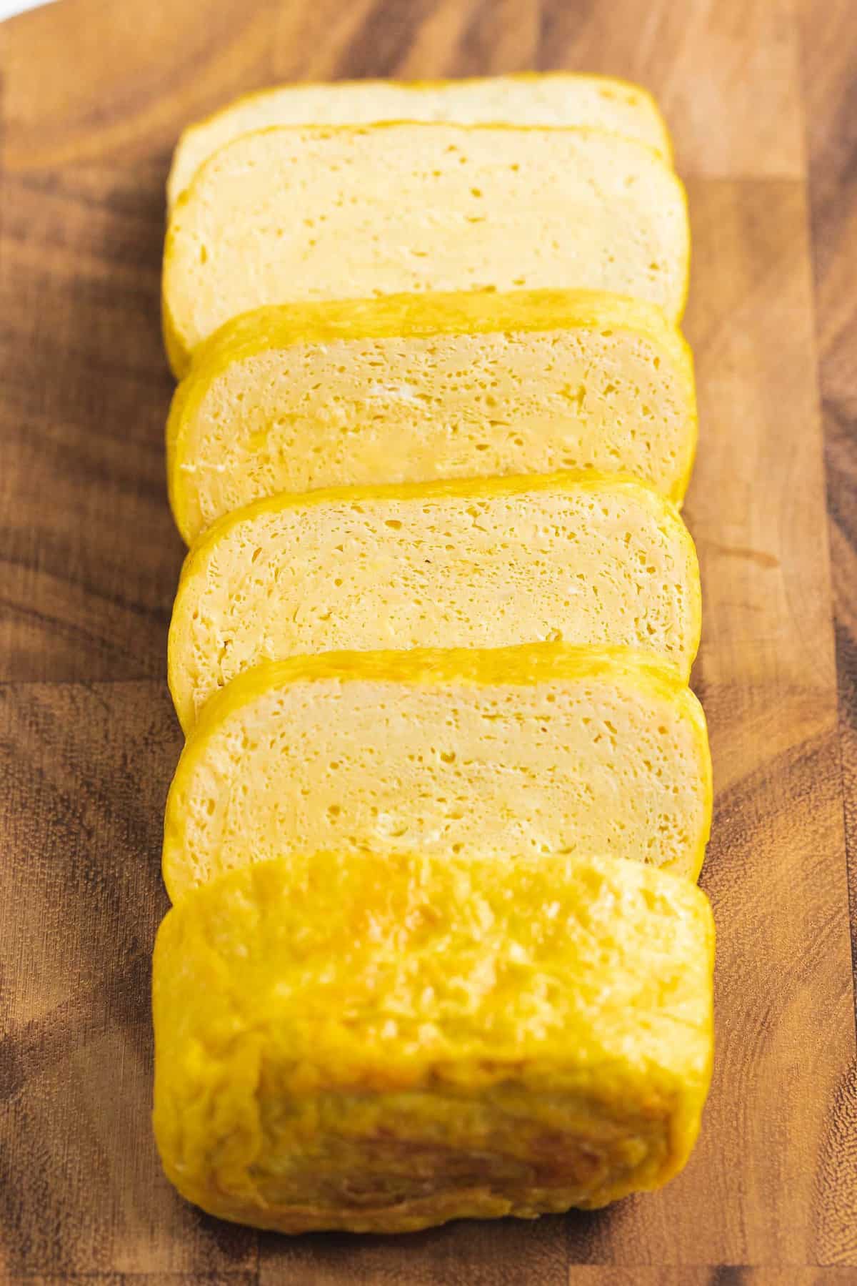 Tamagoyaki rolled omelet sliced on a wooden cutting board.