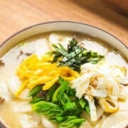 Tteokguk or Korean rice cake soup with text overlay.