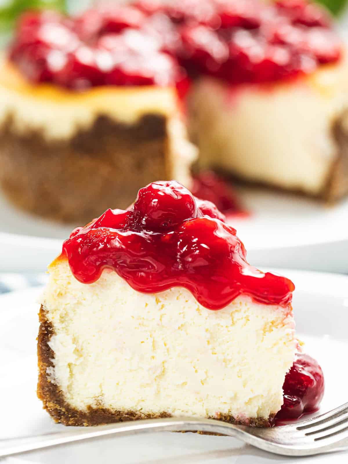 A slice of cherry cheesecake with cherry sauce dripping down.