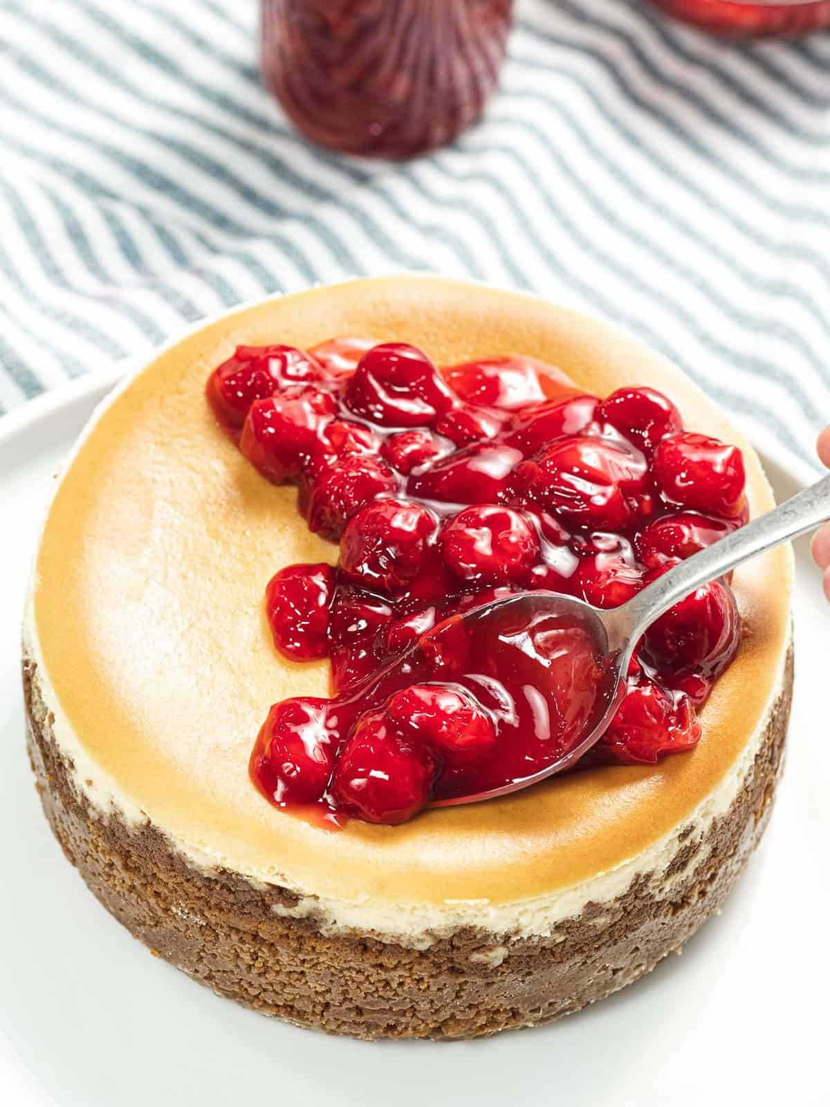 The cherry topping is spooned onto a cheesecake.