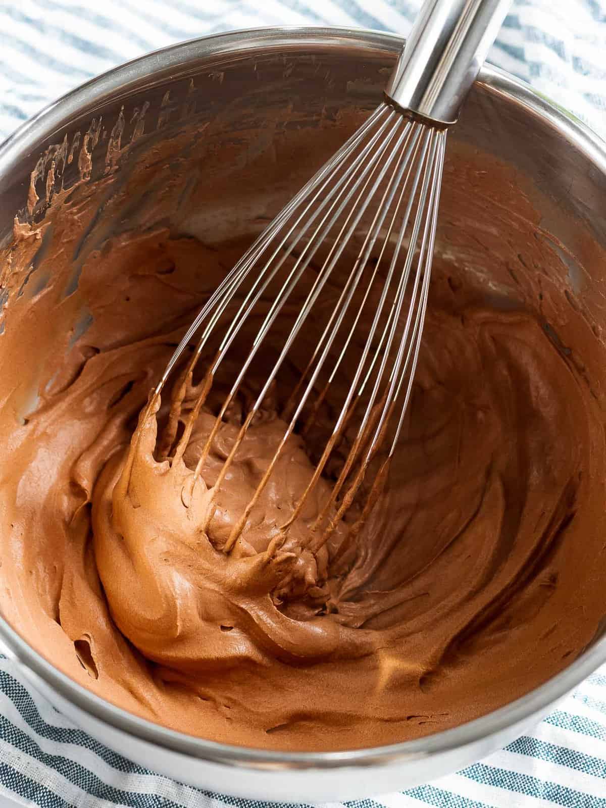 Chocolate whipped cream in a bowl with a whisk.