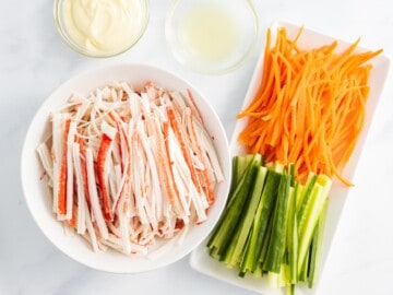Shredded crab stick next to julienned carrots and cucumber.