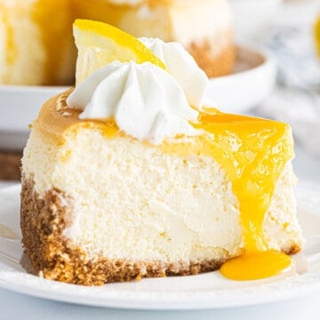 A slice of lemon cheesecake topped with lemon curd, a lemon slice, and whipped cream.