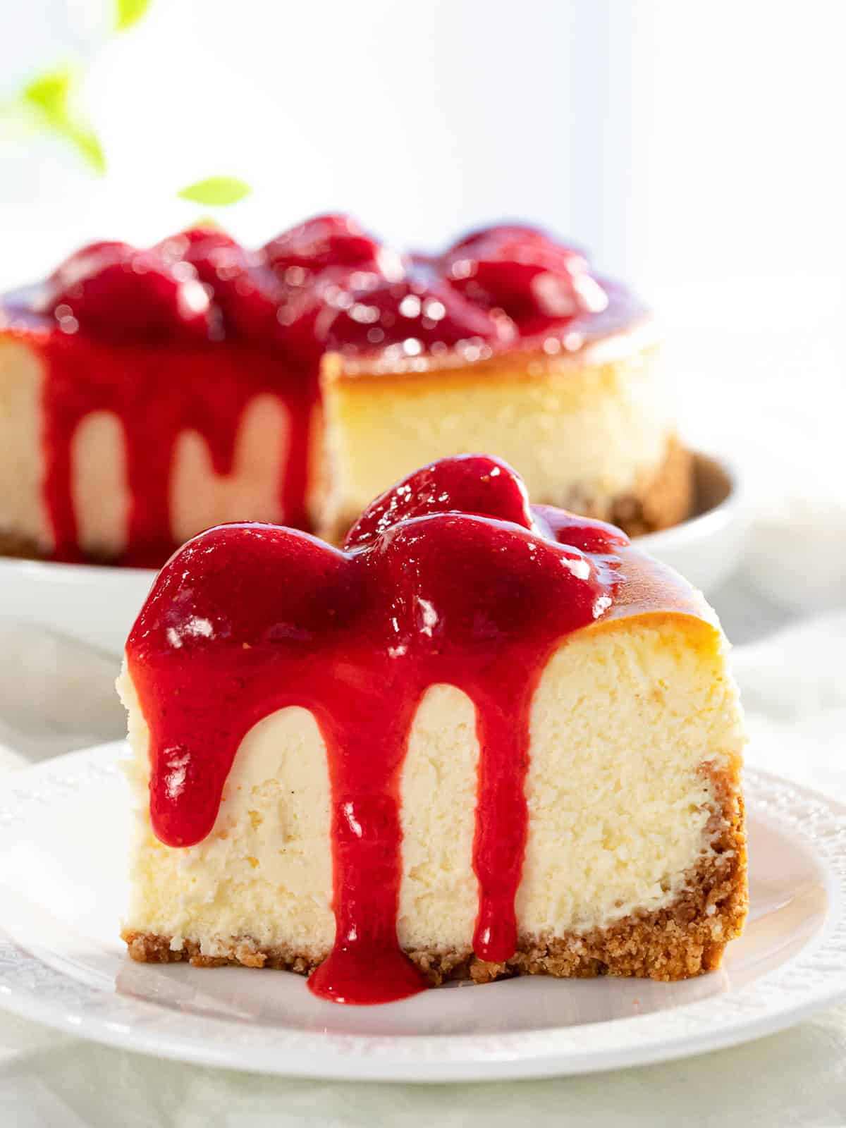 A slice of strawberry cheesecake with strawberry sauce dripping down the sides.