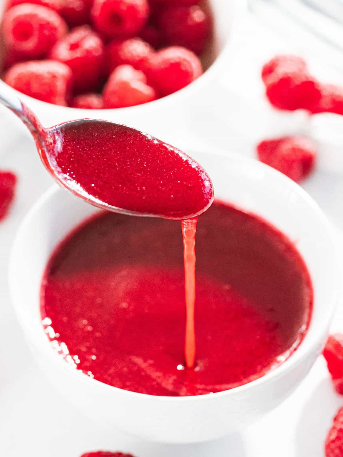 Raspberry sauce poured off a spoon to show smooth texture.